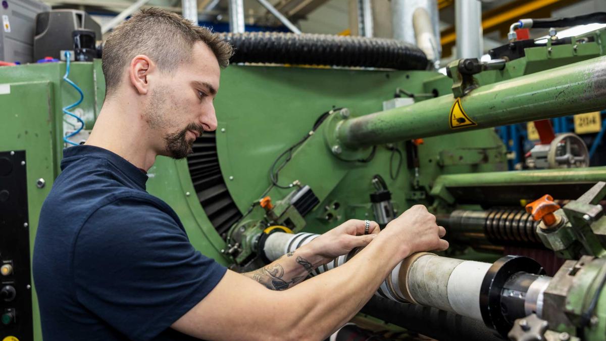 Man in blue shirt working on a machine and looking at his hands