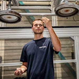 Young man is standing in a production area and working on a machine