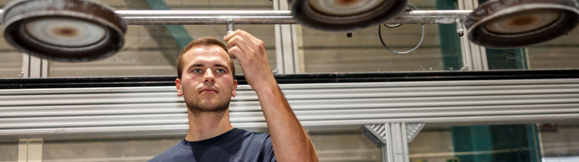 Young man is standing in a production area and working on a machine