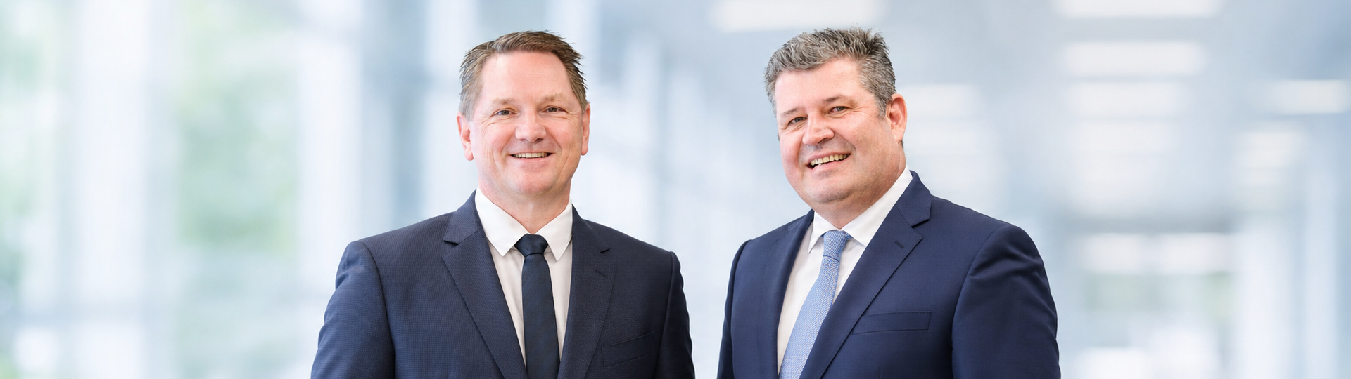 The managing directors of Krempel GmbH are standing against a light-colored background and smiling at the camera.