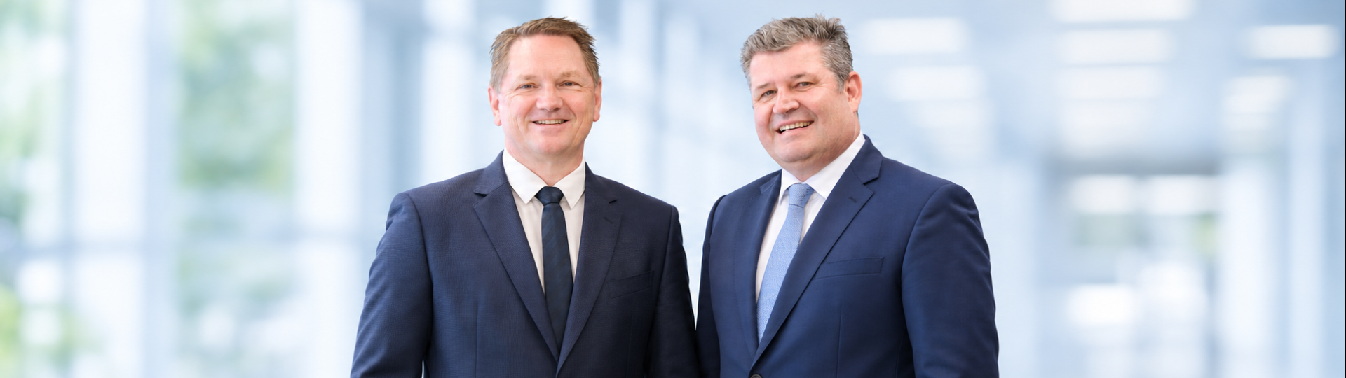 The managing directors of Krempel GmbH are standing against a light-colored background and smiling at the camera.