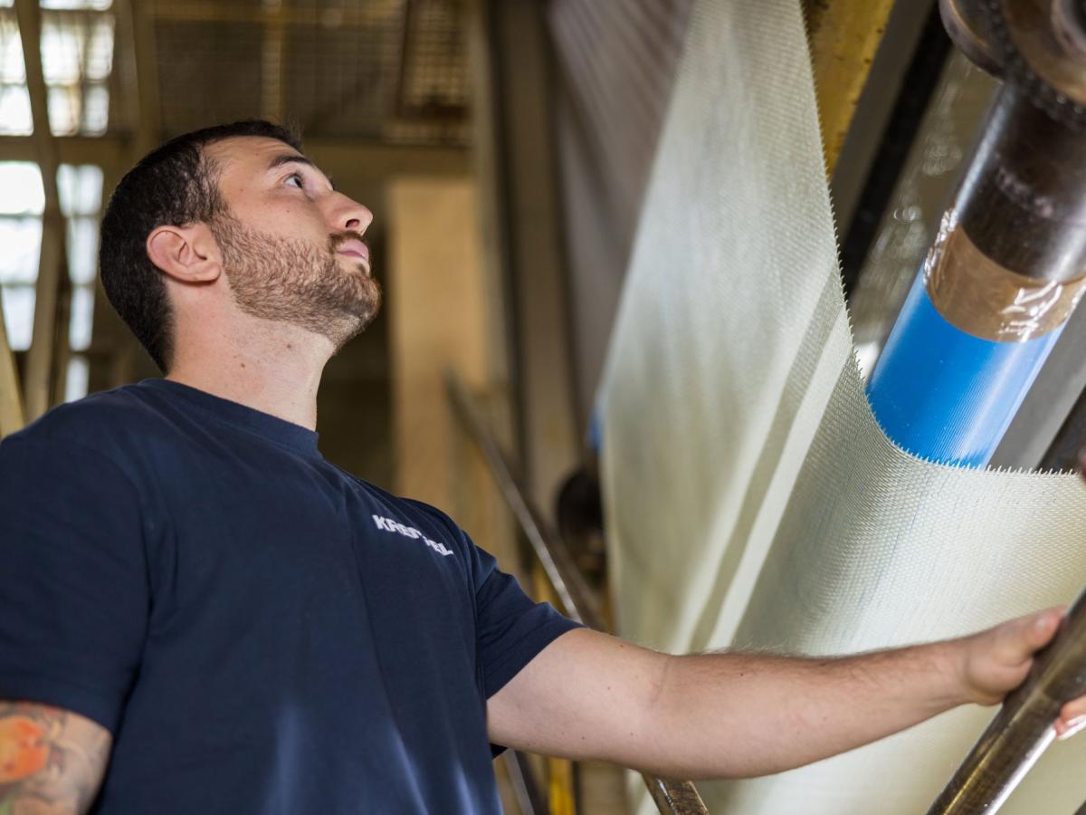 Ein junger Mann steht an einer Maschine an der das Material nach oben fließt