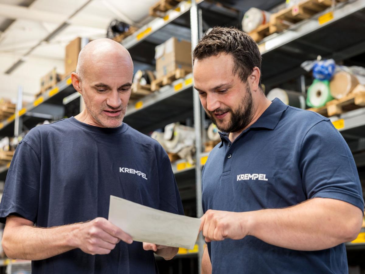 Tow men standing in a warehouse disucssing something while looking at a piece of paper