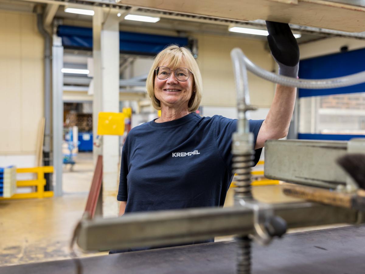 Woman standing in a production area and working on a machine while smiling into the camera