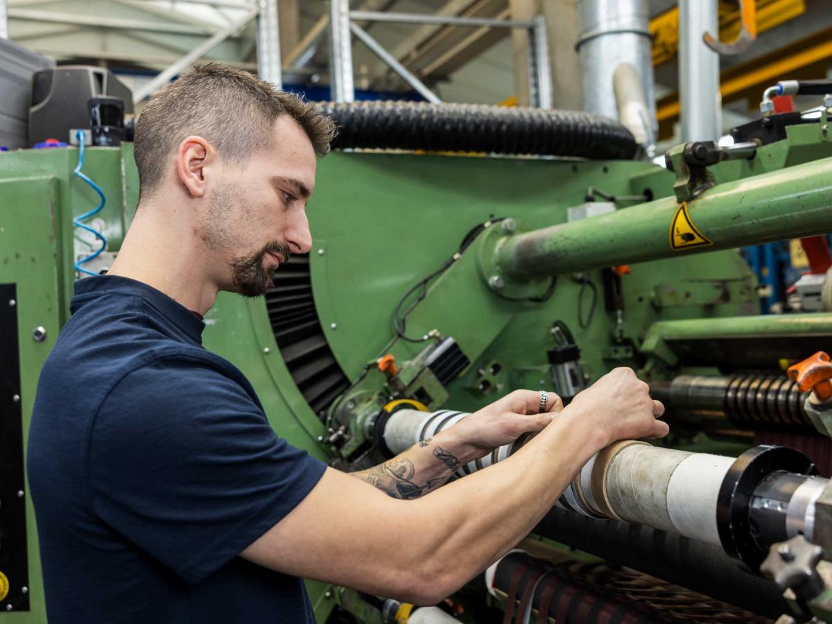 Man in blue shirt working on a machine and looking at his hands