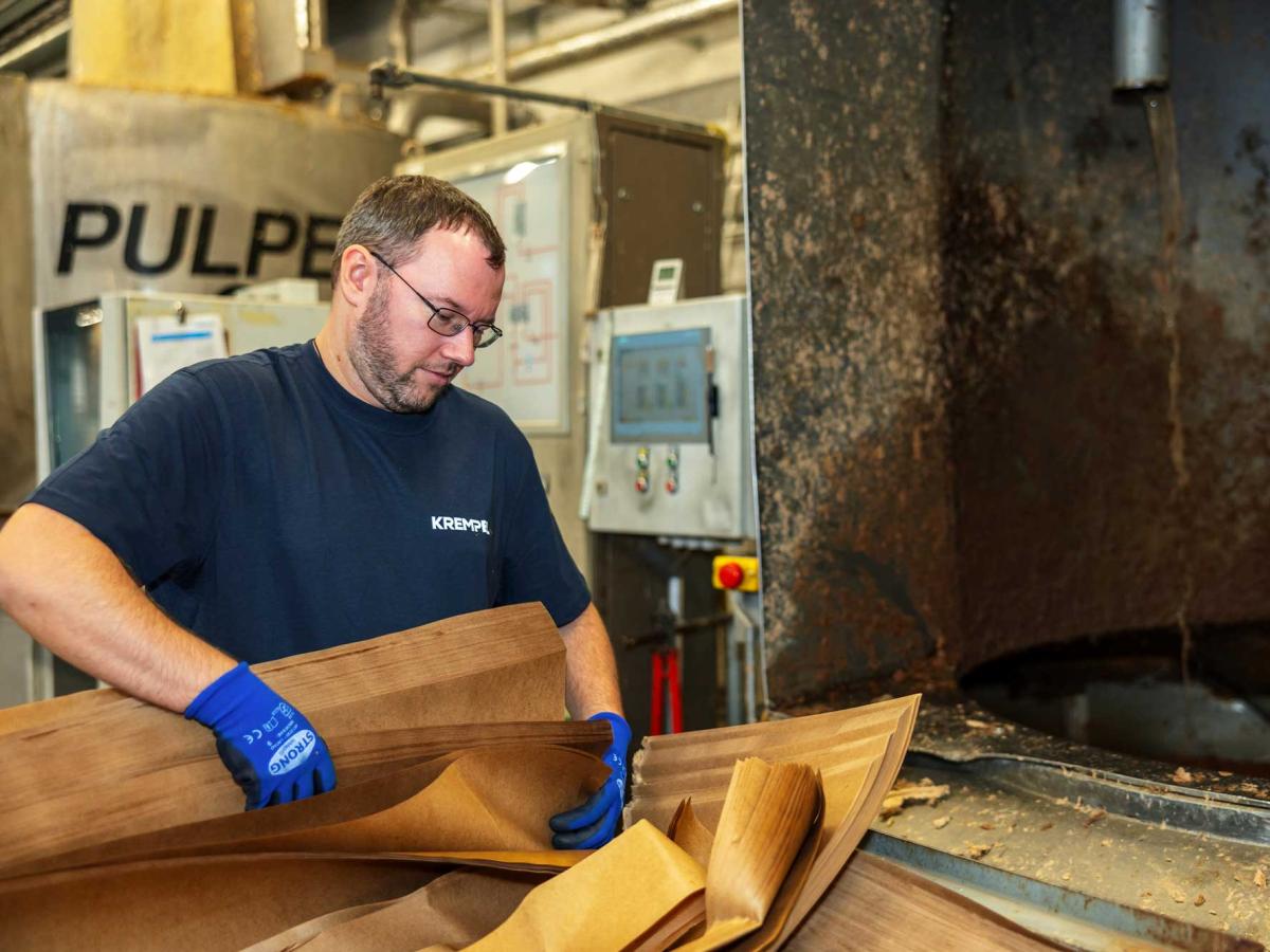 Man with glasses working in a production area and looking at papier that he is putting in a machine