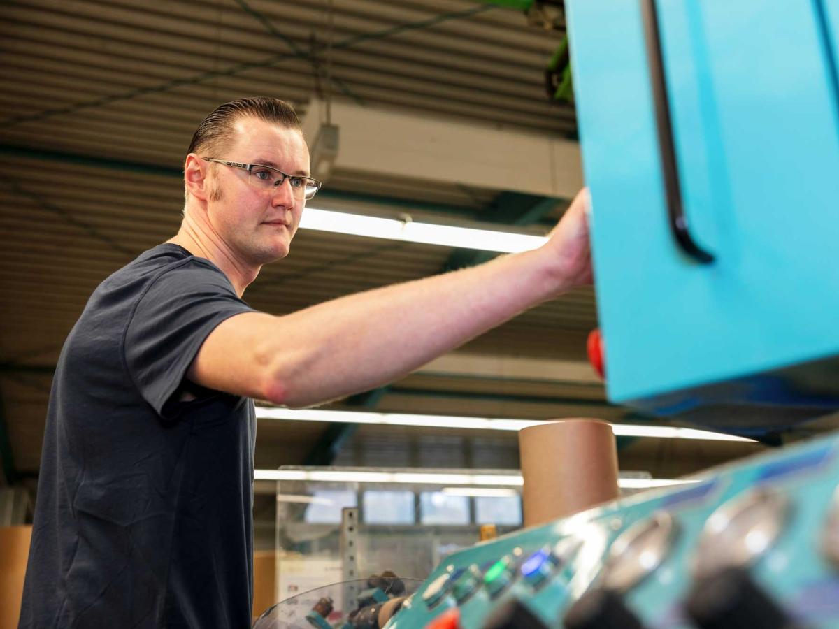 Young man with glasses standing in front of a machine control panel and pressing a button