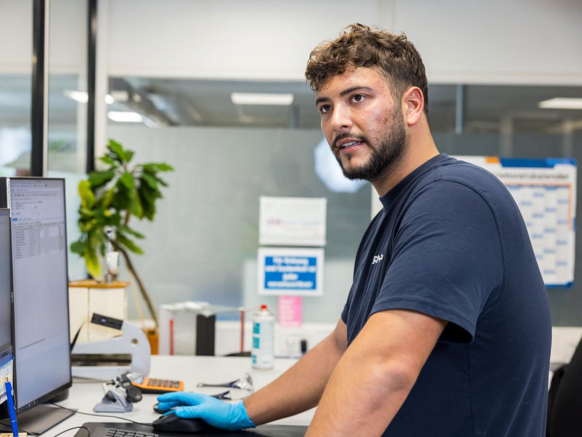 Young man is standing in front of a computer in a lab and looking at the camera
